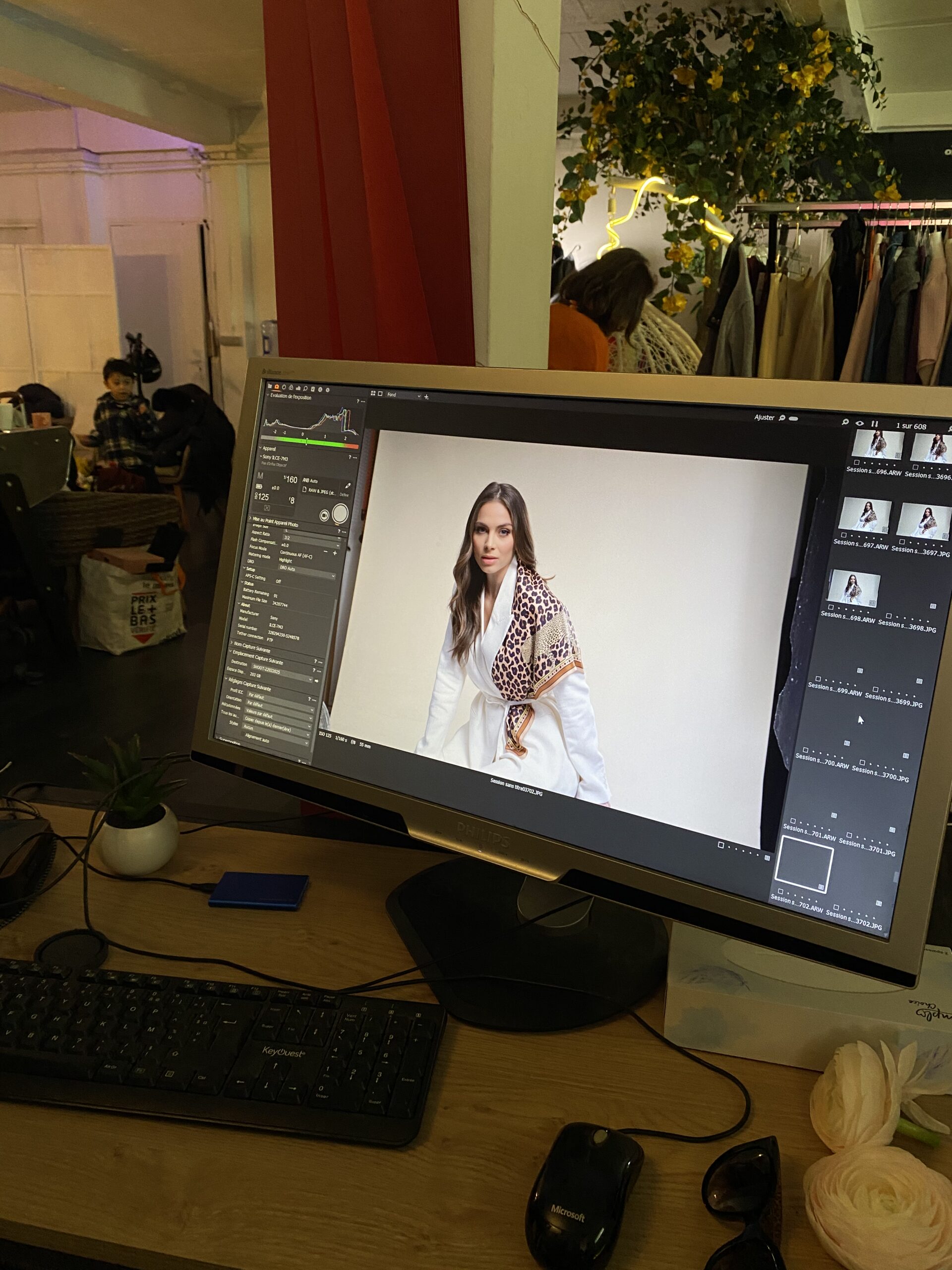 Station de Montage Vidéo – Coulisses d’un Shooting de Mode Vue d'un poste de travail professionnel avec un moniteur Philips affichant un plan de montage vidéo d'un mannequin. Un clavier KeyQuest, une souris et des éléments de studio sont visibles en premier plan et en arrière-plan.