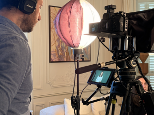Coulisses d'un tournage vidéo corporate dans un salon avec un vidéaste professionnel équipé d'une caméra sur trépied, d'un moniteur de contrôle et d'un éclairage de studio.