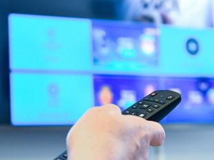 Photographie d'une main qui tient une télécommande pour allumer une télévision